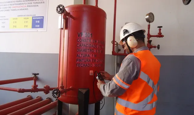 Técnico com colete laranja inspecionando vaso de pressão vermelho VP 501