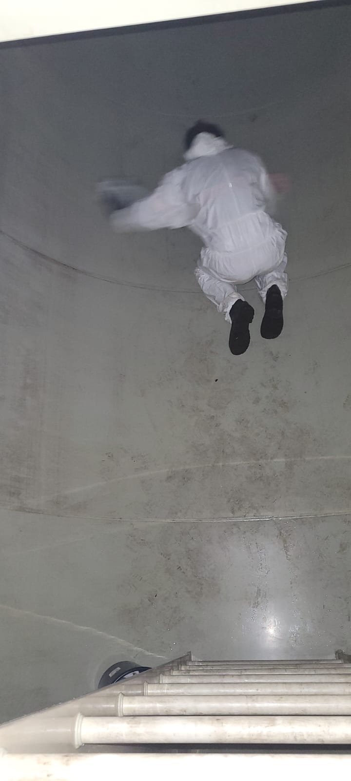 Técnico com macacão branco de proteção dentro de tanque de grande porte